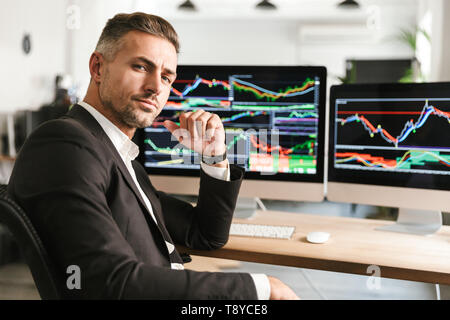 Immagine di imprenditore moderno 30s indossare tuta di lavoro di Office sul computer con grafica e grafici a schermo Foto Stock