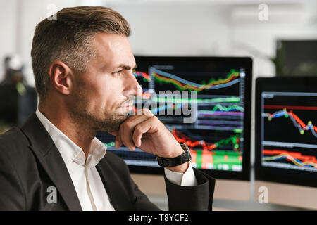 Immagine di imprenditore serio 30s indossare tuta di lavoro di Office sul computer con grafica e grafici a schermo Foto Stock