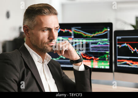 Immagine dell'imprenditore bello 30s indossare tuta di lavoro di Office sul computer con grafica e grafici a schermo Foto Stock