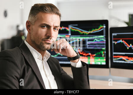 Immagine di imprenditore di successo 30s indossare tuta di lavoro di Office sul computer con grafica e grafici a schermo Foto Stock