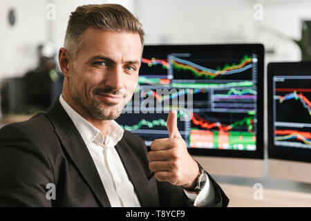 Immagine dell'imprenditore europeo 30s indossare tuta di lavoro di Office sul computer con grafica e grafici a schermo Foto Stock
