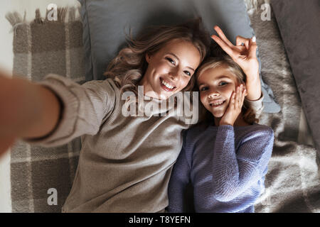 Immagine di un felice giovane donna con la sua sorellina al chiuso in casa prendere un selfie dalla telecamera. Foto Stock