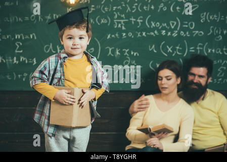 I genitori in ascolto il loro figlio, controllo errori con prenota lavagna sullo sfondo. Ragazzo presentando la sua conoscenza a mamma e papà. Smart bambino in Foto Stock