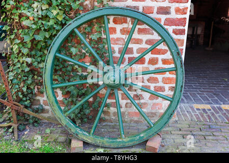 Il vecchio cavallo ruota carrello con verde sfald vernice di rivestimento appoggiata contro un muro in mattoni. Foto Stock