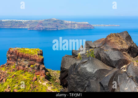 Santorini, Grecia panorama con Skaros rock, grande pietra vulcanica e caldera, mare, fiori e isola di Vulcano sullo sfondo Foto Stock
