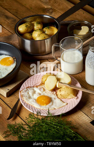 Uovo fritto con giovani di patate con aneto e latte sul tavolo di legno Foto Stock