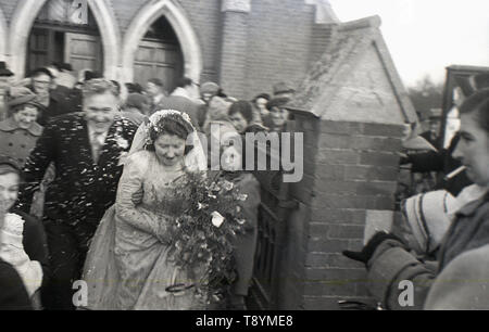 Degli anni Cinquanta, storico, dopo il servizio di nozze, la sposa e lo sposo dash per il loro trasporto dopo aver coperto con la celebrazione conffetti alle porte della chiesa, Inghilterra, Regno Unito. Foto Stock