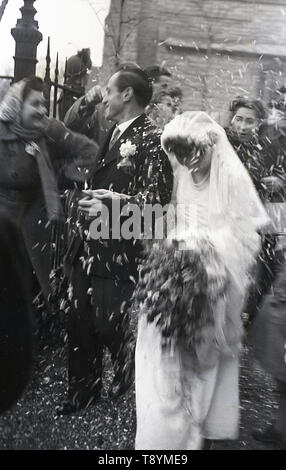 Degli anni Cinquanta, storico, dopo il servizio di nozze, vediamo che la sposa e lo sposo facendo la doccia o ricoperti di coriandoli gettati da gli ospiti alle porte della chiesa, Inghilterra, Regno Unito. Foto Stock