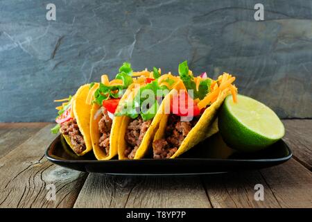Disco sgusciate tacos con carne di manzo macinata, lattuga, pomodoro e formaggio. Gruppo sulla piastra con uno sfondo scuro. Foto Stock