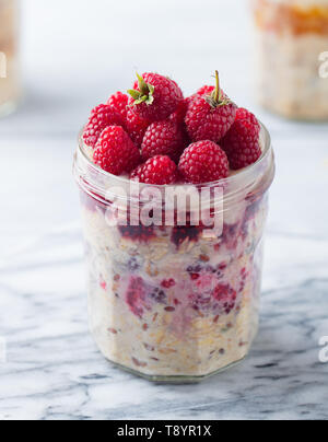 Per una notte di avena, bircher muesli con lampone in un vasetto di vetro su sfondo marmo. Close up. Foto Stock