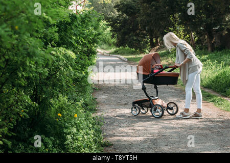 Bella giovane madre con un bambino trasporto passeggiate nel parco in primavera Foto Stock