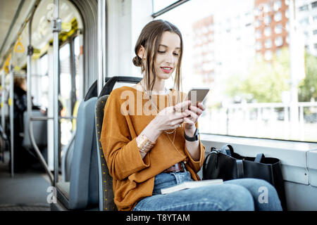 Giovane e donna felice utilizza lo smartphone mentre è seduto vicino alla finestra nel trasporto pubblico durante il viaggio Foto Stock