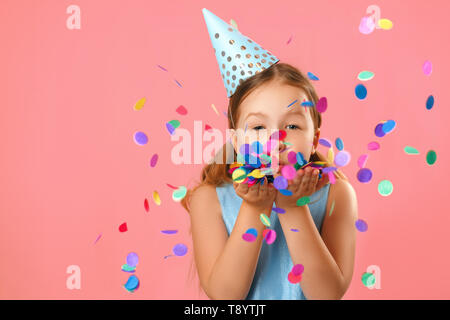 Allegro bambina festeggia il compleanno. Il bambino si brucia coriandoli dalle mani. Primo piano verticale sul corallo rosa sfondo. Foto Stock