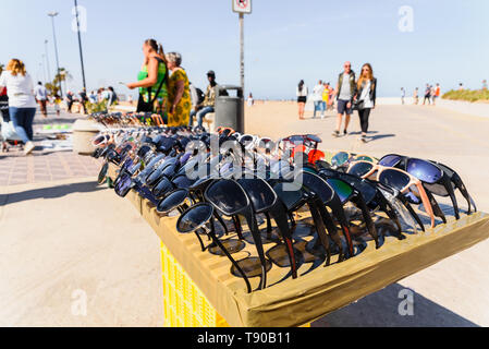 Valencia, Spagna - 12 Maggio 2019: gli immigrati clandestini vendita di occhiali falsi e negozio di souvenir per i turisti sulla spiaggia di Valencia. Foto Stock
