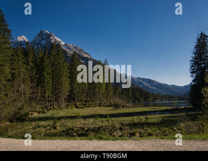 Un sentiero di ghiaia sulla riva del Hintersee a Berchtesgaden con la foresta e la montagna Foto Stock