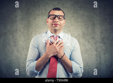 Uomo d'affari con gli occhi chiusi tiene le mani sul petto vicino al cuore, mostra la gentilezza, esprime sincere emozioni, essendo natura generosa. Il linguaggio del corpo sentimenti Foto Stock