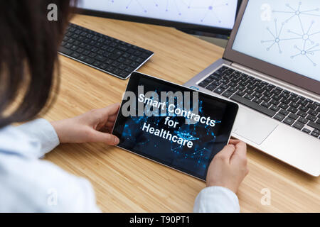 Femmina di business utilizzando Smart Contratti per la sanità. Illustrazione di Ethereum Blockchain sullo schermo del Tablet PC e laptop. Foto Stock