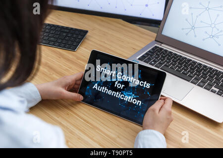 Femmina di business utilizzando Smart contratti per l'autenticazione. Illustrazione di Ethereum Blockchain sullo schermo del Tablet PC e laptop. Foto Stock