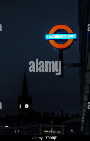 Illuminato segno della metropolitana con la torre della stazione di St Pancras in background, London, Regno Unito Foto Stock