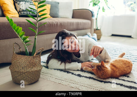 Giovane donna giocando con il gatto sul tappeto a casa. Master giacente sul piano con il suo animale domestico Foto Stock