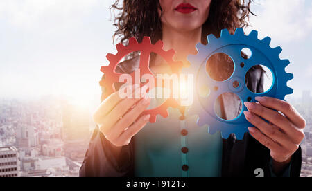 Imprenditrice tenta di collegare pezzi di ingranaggi. Concetto di lavoro di squadra, il partenariato e l'integrazione. Foto Stock