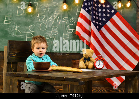 Si torna a scuola o scuola. Felice giorno di indipendenza degli Stati Uniti d'America. Little Boy mangiare pane a bandiera americana a conoscenza giorno. Scuola kid a lezione Foto Stock