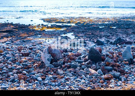 Piccole pietre su una spiaggia nera, in background sono akean onde e un surfer Foto Stock