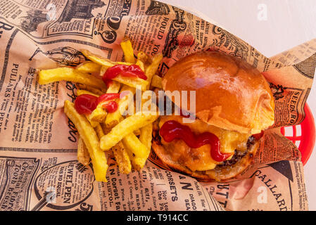 Cheeseburger e patate fritte con ketchup avvolti in un giornale Foto Stock