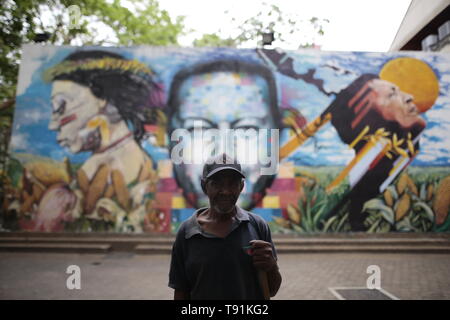 13 maggio 2019, Venezuela, Caracas: Alain Jose Kei, 77 anni, spazzatrice sta di fronte ad un murale con la foto del compianto Presidente Hugo Chavez. "Non abbiamo mai pagato in pieno. La banca non spende tutto su di noi", dice l'uomo che è stato in questa professione per sette anni. Nonostante la situazione, Alain rimane ottimista. " Ho una sensazione è sempre meglio. E continuerò a lavorare perché non voglio perdere questo lavoro", afferma. Il Venezuela è stato in una profonda crisi economica per anni. In un indice, il paese si è classificato di 188 su 190 paesi nel 2018. Che cosa rende Alein godere h Foto Stock