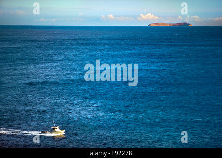 Barca da pesca si muove attraverso il mare passato un'isola all'orizzonte. Foto Stock