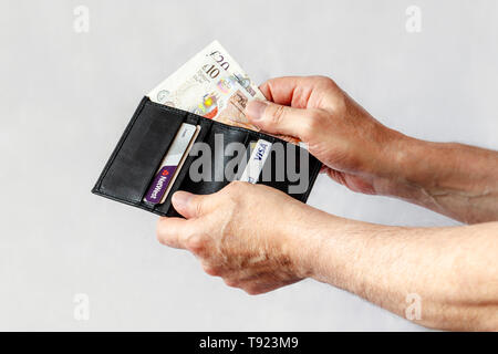 Close-up di un uomo con le mani in mano tenendo una ten-pound e venti-pound nota da un nero portafoglio in pelle, contenente anche le carte di credito Foto Stock