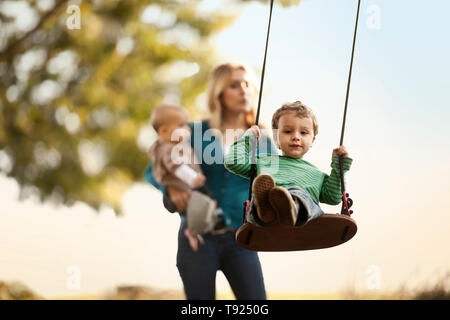 Ragazzo giovane essendo spinto da sua madre su un albero di rotazione. Foto Stock