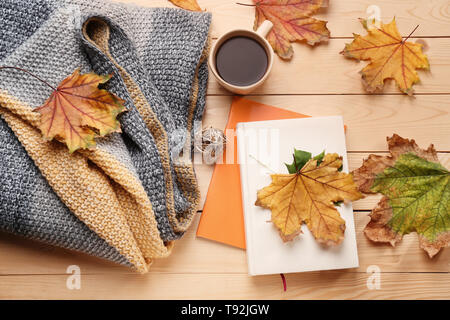 Composizione con tazza di delizioso vino brulé, caldi plaid, libri e foglie di autunno su sfondo di legno Foto Stock