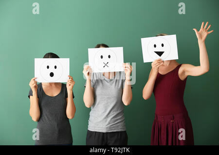 Giovani donne volti nascosti dietro i fogli di carta con le emoticon disegnata sul colore di sfondo Foto Stock