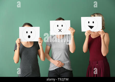 Giovani donne volti nascosti dietro i fogli di carta con le emoticon disegnata sul colore di sfondo Foto Stock