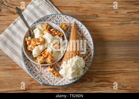 Cono di cialda con deliziosi gelati e popcorn su piastra Foto Stock