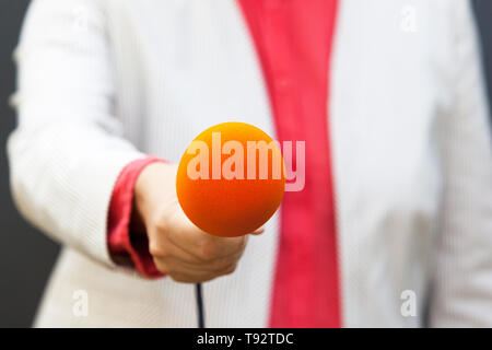 Reporter femmina tenendo il microfono, rendendo intervista Foto Stock