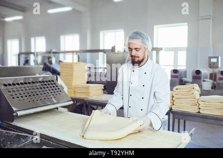 Un panettiere con la barba rende l'impasto sulle apparecchiature in forno per fare il pane. Foto Stock