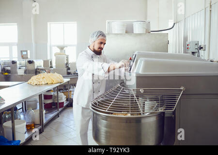 Un panettiere con la barba rende l'impasto sulle apparecchiature in forno per fare il pane. Foto Stock