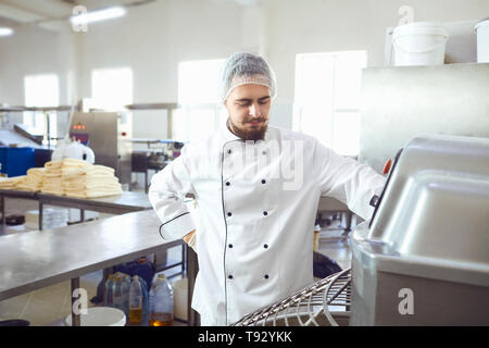 Un panettiere con la barba rende l'impasto sulle apparecchiature in forno per fare il pane. Foto Stock