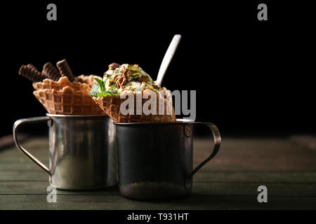 Coppe in metallo con disegno waffle coni e deliziosi gelati sul tavolo di legno Foto Stock