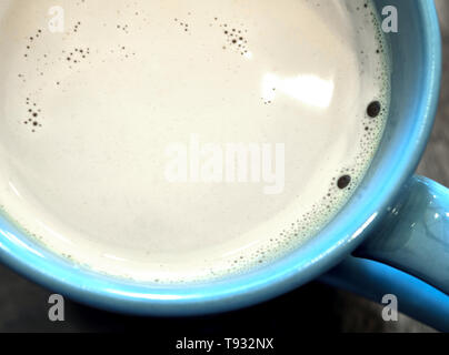 Caffè latte in una tazza di colore blu sul legno e vetro superiore tabella Foto Stock