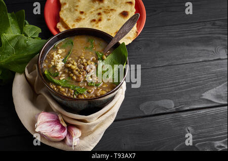 Mung Dhal con spinaci, Chapati e aglio in nero da tavolo in legno. Moong Dal - Cucina Indiana curry. Vegetariano piatto piccante. Spazio di copia Foto Stock