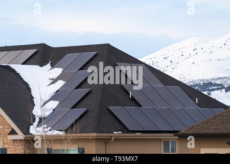 Pannelli solari installati sul tetto scuro di una casa con la neve in inverno Foto Stock