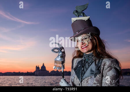 Ritratto di una donna mascherata in un bellissimo costume di creative, ponendo sulla isola di San Giorgio di Maggiore, celebra il Carnevale veneziano, Basilica Foto Stock