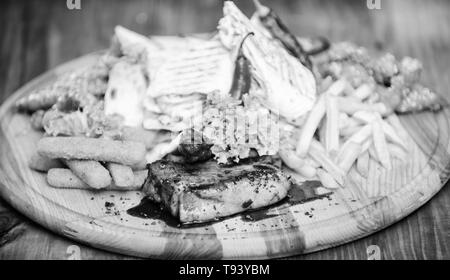 Snack per la birra. Tavola di legno patatine fritte bastoncini di pesce burrito e bistecca di carne con insalata mista. Pub menu snack. Godetevi il vostro pasto. Spuntino a base di carne per il gruppo amici. Gustosi spuntini deliziosi. Il cibo del ristorante. Foto Stock