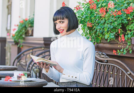 Ragazza bere il caffè leggere il libro. La tazza di un buon caffè e libro piacevole combinazione migliore per un perfetto fine settimana. Miglioramento di auto concetto. La donna bere godono di un buon libro cafe terrazza. La letteratura per femmina. Foto Stock