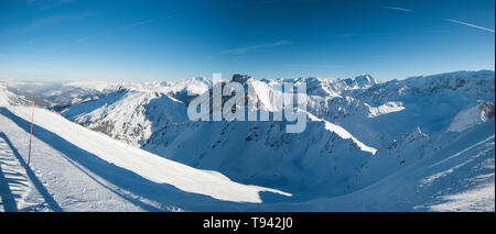 Vista panoramica verso il basso coperto di neve valle nella catena montuosa alpina sul cielo blu sullo sfondo Foto Stock