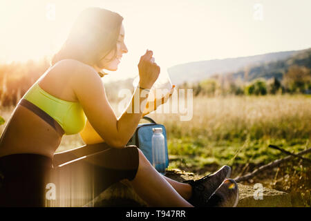 Giovane donna sportivo mangiare sano il pranzo nel campo al tramonto Foto Stock