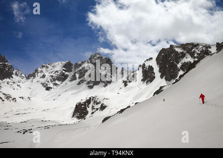 Coperta di neve mountain range con tracce di valanghe, soleggiato cielo nuvoloso ed escursionisti in rosso con il cane sul pendio nevoso. Turchia, Kachkar montagne, parte alta Foto Stock